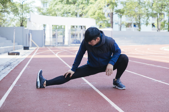 运动亚泰男子在黑色运动服伸展腿热身前准备慢跑或在体育场跑步。