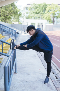 运动亚泰男子在黑色运动服伸展腿热身前准备慢跑或在体育场跑步。
