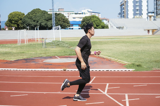 运动亚泰男子身穿黑色运动服慢跑或在体育场内跑道上跑步。