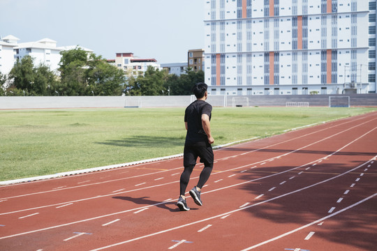 运动亚泰男子身穿黑色运动服慢跑或在体育场内跑道上跑步。