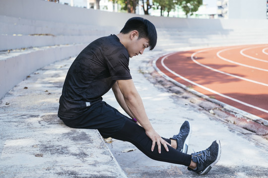 身穿黑色运动服的亚泰男子在体育场内运动后休息。