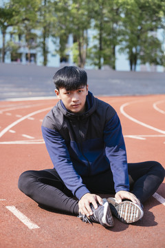 运动亚泰男子身穿黑色运动服坐在跑道上。