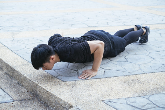 穿黑色运动服的运动型男子在地上做俯卧撑。