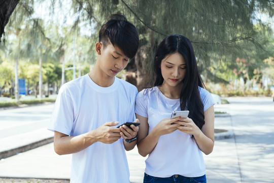 一对青少年站在公园里，用智能手机在社交媒体上冲浪。