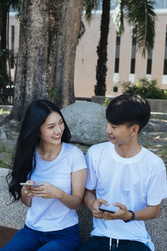 一对情侣坐在公园里，一边约会一边在社交媒体上冲浪。