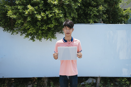 男人和女人穿着粉红色的T恤衫站在白色的墙上，拿着一张空白纸作为复印空间。