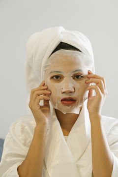 穿着白色浴袍的年轻女子摘下脸上的化妆面具。