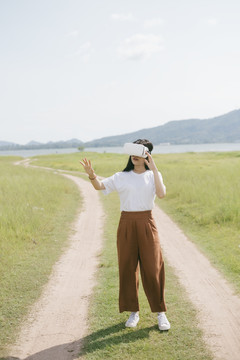 黑色长发女子穿着休闲服，戴着VR护目镜，在泥泞的草原上行走，享受虚拟现实技术。