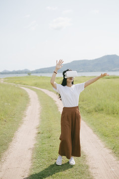 黑色长发女子穿着休闲服，戴着VR护目镜，在泥泞的草原上行走，享受虚拟现实技术。