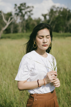 穿着休闲服的黑色长发女子，在风和日丽的日子里，静静地站在草地上，捧着野草。