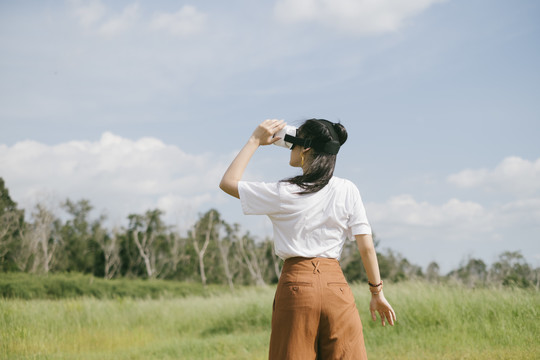 黑色马尾头发的女人穿着休闲服，戴着VR护目镜，在泥泞的草地上旅行，享受虚拟现实技术。