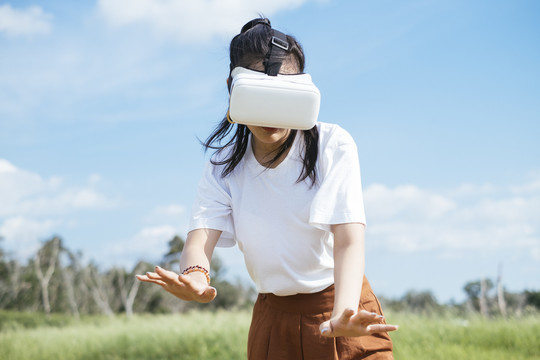 黑色马尾头发的女人穿着休闲服，戴着VR护目镜，在泥泞的草地上旅行，享受虚拟现实技术。
