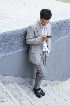 穿着正装的聪明亚泰商人在户外楼梯上使用智能手机。