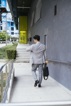 后视图-聪明的亚泰商人在正式西装看手表走在户外下班后。