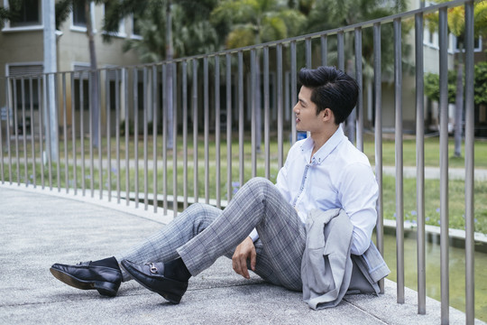 聪明的亚泰商人穿着白领衬衫，坐在公园户外的地板上休息。