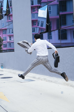 后视图-聪明的亚泰商人穿着白领衬衫，工作结束后在户外跳跃。