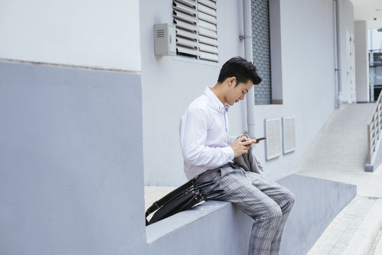 聪明的亚泰商人穿着白领衬衫坐在户外使用智能手机。