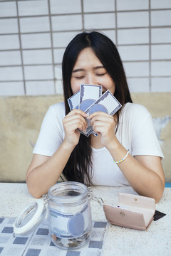 黑色长发女孩感激她存钱的同时，她数着钱，闻着钱的味道。