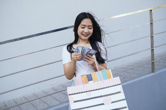 黑色长发女孩拿着很多购物回来数钞票购物后检查左边的余额。