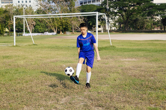 那个小足球运动员在操场上独自练习足球技术。