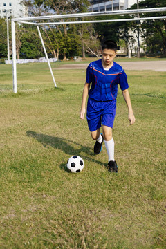 穿着蓝色足球服的小男孩独自练习足球技术。