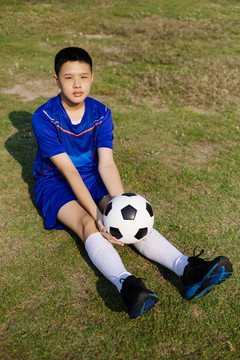 一个男孩坐在草地上，手里拿着球。