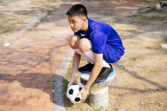 一个男孩手拿足球坐在人行道旁的一根杆子上。
