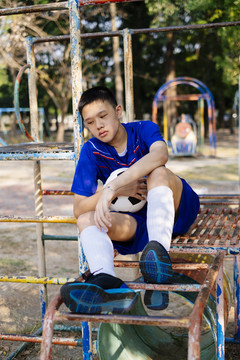 一个小足球运动员在操场上的土管上休息，一边练习他的足球技术。