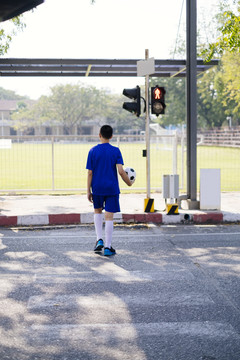 一个男孩在斑马线上踢足球过马路。