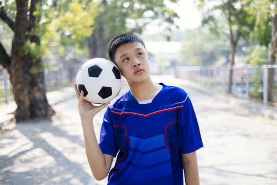 一个机器人站在公园里，在他的头旁边举起足球。