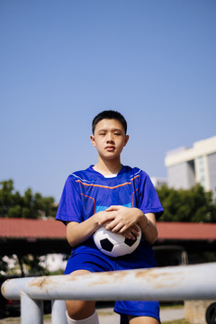 一个男孩坐在扶手上，手里拿着足球的肖像照。