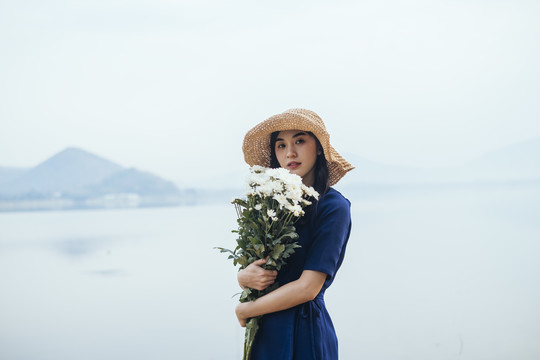 一个美丽的泰国女孩站在湖边，抱着白色的花朵，直直地看着。