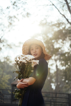 美丽的泰国女孩抱着白花站在森林里。