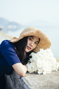 美丽女孩把头靠在水坝路障上的白花上的肖像照。