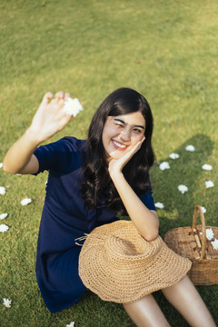 一头卷曲长发的深蓝色女孩坐在田野里，把白色的花举向阳光。