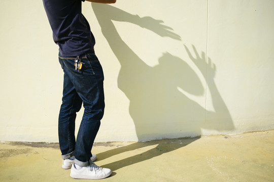 一个男人站在阳光下，背影在墙上的剪影。