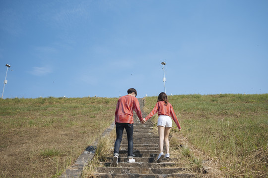 一对身穿红色t恤的年轻夫妇手牵着手，走上通向蓝天和光明未来的楼梯。