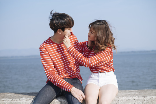 身着红色t恤的年轻情人坐在大坝的路障上，互相挤压脸颊。