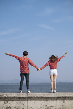 一对年轻的夫妇站在大坝的路障上，相互握着一只手，向天空举起另一只手。