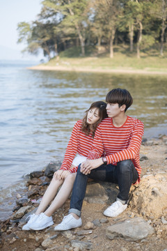 一对穿着红色t恤的年轻夫妇坐在森林里湖边的岩石上。