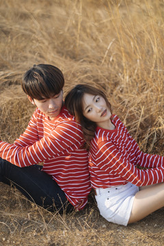 一对年轻夫妇背靠背坐在草地上的特写镜头。