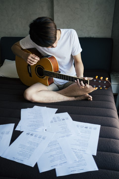 年轻的泰国吉他手在卧室练习原声吉他。读音乐抒情纸。