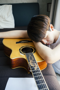 年轻的泰国吉他手男子睡在卧室里的原声吉他。
