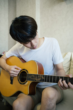 特写镜头：穿着白衬衫的泰国吉他手在客厅的沙发上弹原声吉他。