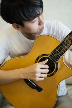 年轻的泰国吉他手在家的沙发上弹原声吉他。