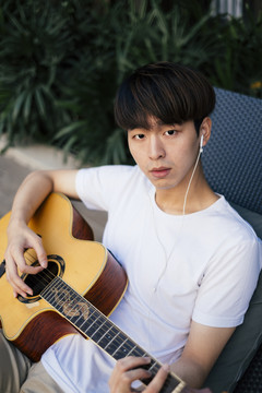 年轻的泰国吉他手的肖像男子用耳机听音乐和弹原声吉他。