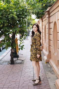 一头卷曲的长发，穿着黄色衣服的女孩走在有橘黄色墙和树的小径上。