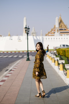 可爱的卷发黄裙女孩走在人行道上，走向寺庙。
