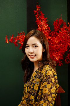 可爱的卷发黄裙女孩站在绿色的墙前，红色的花。