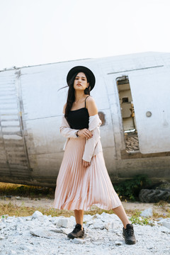 一位身穿黑色和粉色衣服的长发女子站在失事飞机前，穿着粉色西装露出肩膀，闭上嘴。